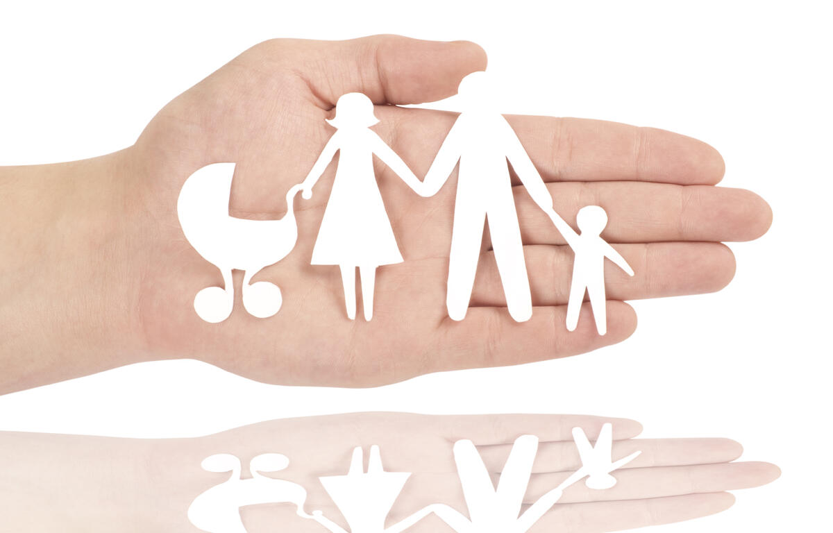 Paper cutout of a family in the palm of a hand.