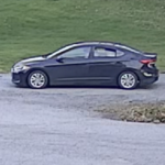 Dark blue four-door sedan parked on a gravel lot with a grassy embankment in the background.