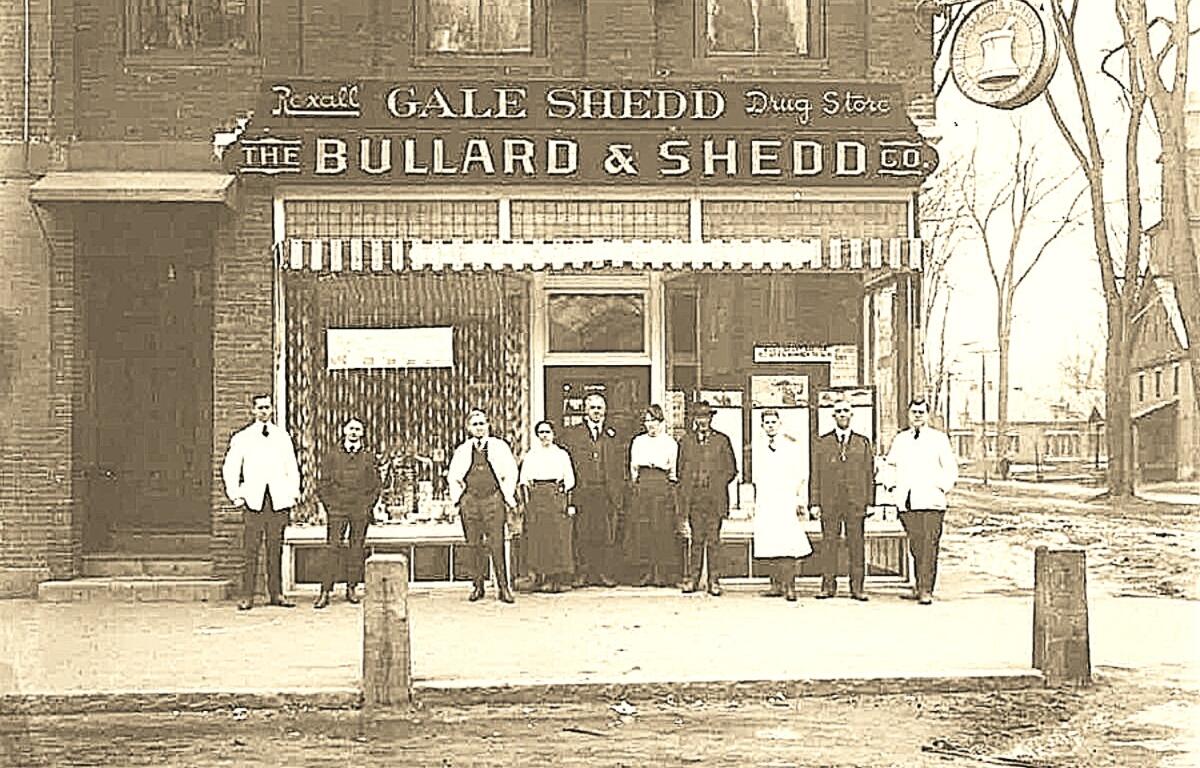 Historic sepia photo of a storefront reading 'The Bullard & Shedd Co' with a group of men and women posing outside on a city street, early 20th century attire.
