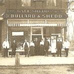 Historic sepia photo of a storefront reading 'The Bullard & Shedd Co' with a group of men and women posing outside on a city street, early 20th century attire.