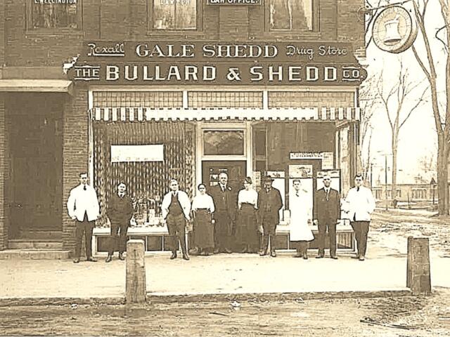 Historic sepia photo of a storefront reading 'The Bullard & Shedd Co' with a group of men and women posing outside on a city street, early 20th century attire.