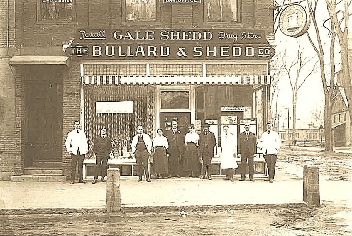 Historic sepia photo of a storefront reading 'The Bullard & Shedd Co' with a group of men and women posing outside on a city street, early 20th century attire.