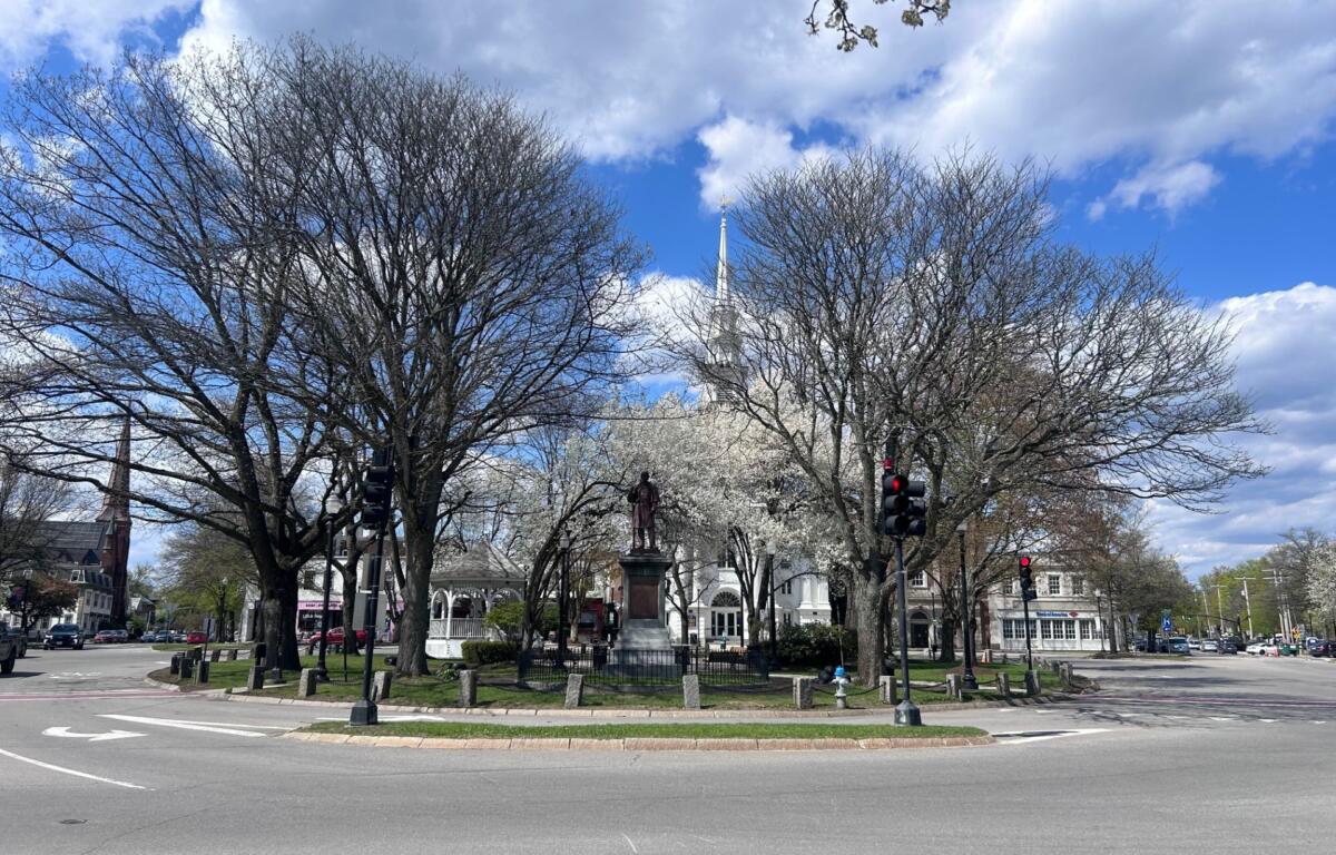 Roundabout plaza with a statue in the center, surrounded by bare trees and a blue sky with clouds.