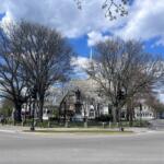 Roundabout plaza with a statue in the center, surrounded by bare trees and a blue sky with clouds.
