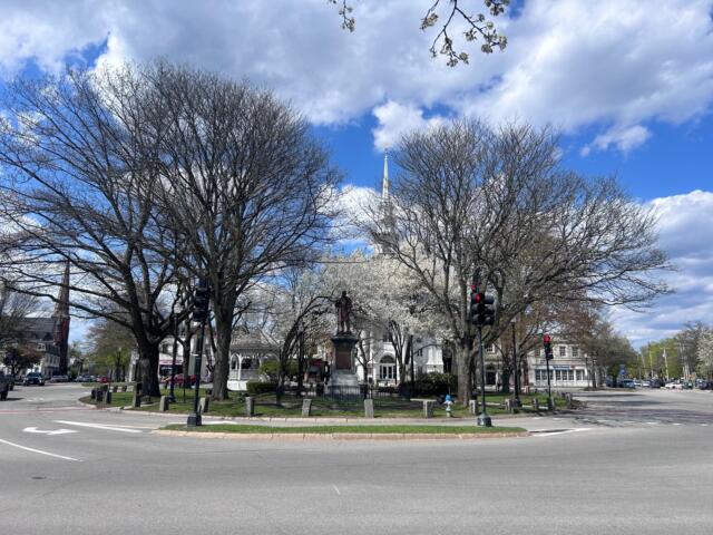 Roundabout plaza with a statue in the center, surrounded by bare trees and a blue sky with clouds.