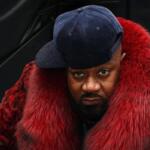Man wearing a blue cap and a bright red fur coat, looking directly at the camera.