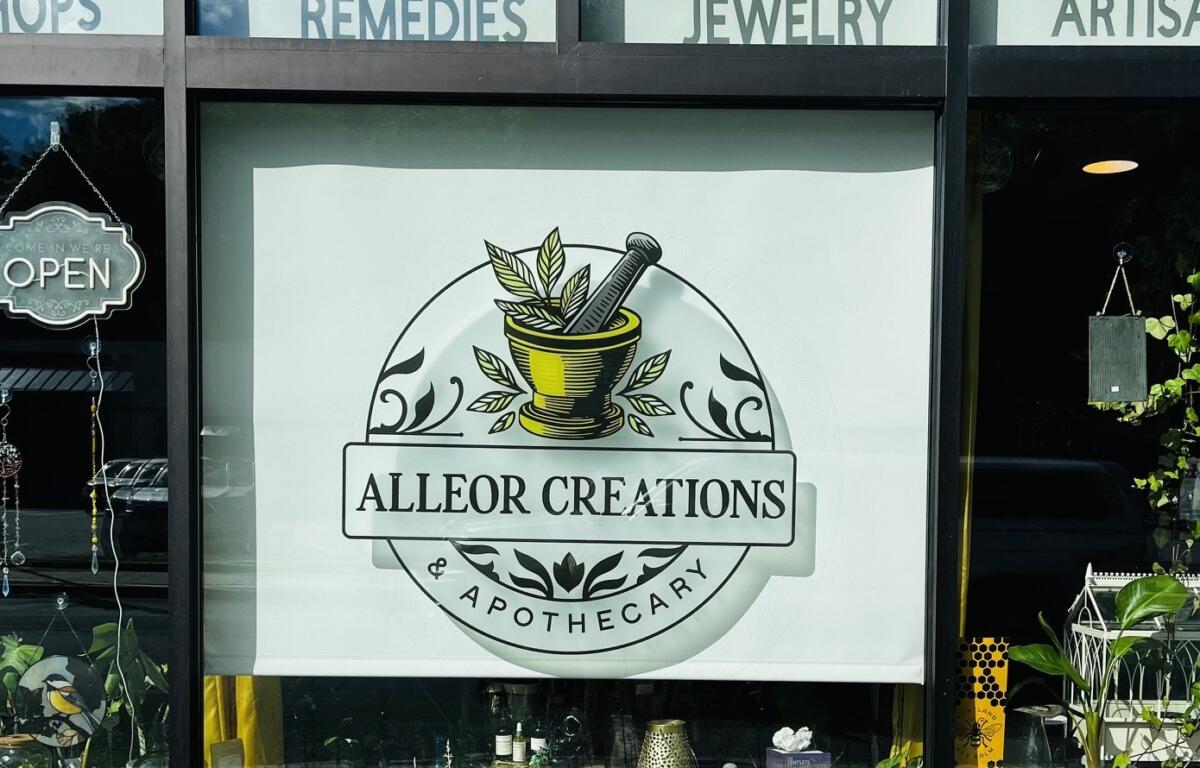 Storefront window display for Alleor Creations Apothecary featuring a circular logo with a mortar and pestle, leaves, and the text 'ALLEOR CREATIONS' and 'APOTHECARY'