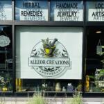 Storefront window display for Alleor Creations Apothecary featuring a circular logo with a mortar and pestle, leaves, and the text 'ALLEOR CREATIONS' and 'APOTHECARY'