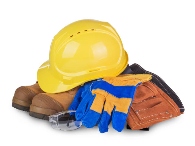 Yellow hard hat atop brown work boots with blue and yellow gloves, safety glasses, and a brown tool pouch stacked together.